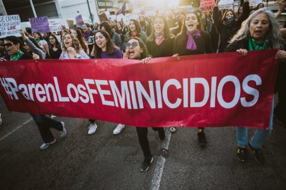 Grupo de mujeres sosteniendo apasionadamente una pancarta que dice "#parenlosfeminicidios" durante una marcha de protesta.