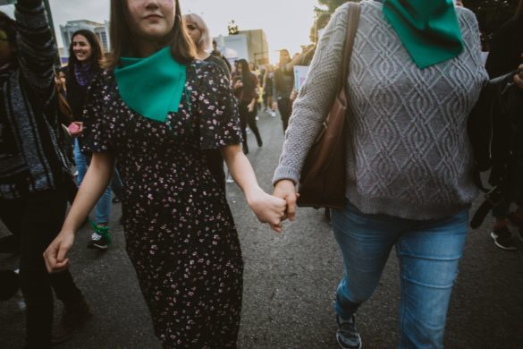 Dos mujeres se toman de la mano en una protesta y caminan entre la multitud junto con otras que llevan pañuelos verdes.